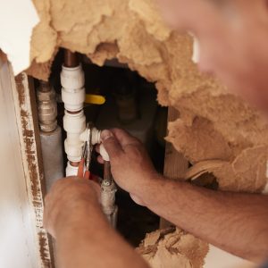 Over shoulder view of middle aged man repairing burst pipe Plumbers working on pipes