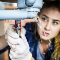 Woman fixing kitchen sink Emergency Plumbers fixing water leaks